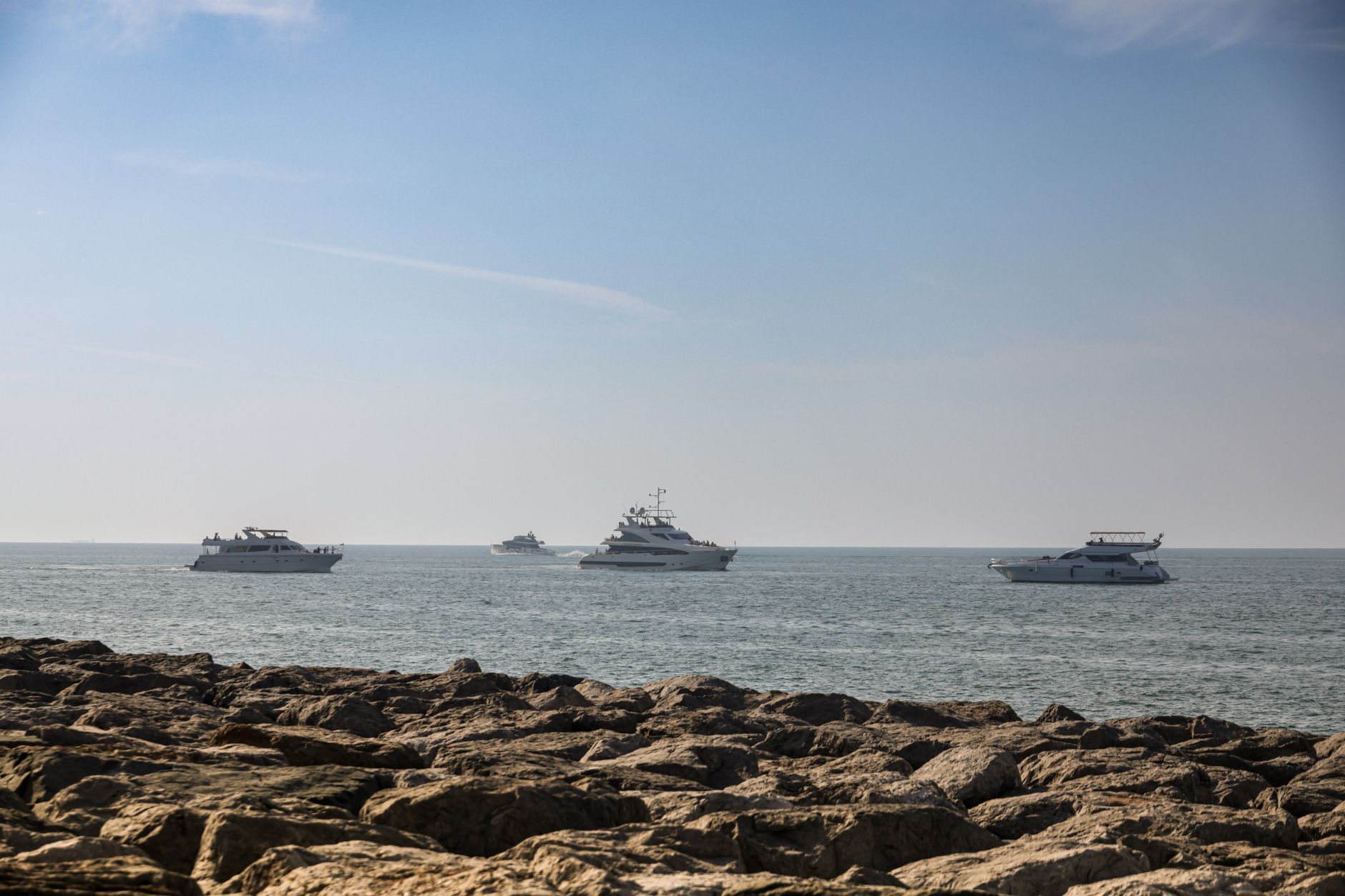 A fleet of luxury yachts sailing on a calm sea near a rocky coastline under a clear blue sky. — photograph by Magda Ehlers on Pexels